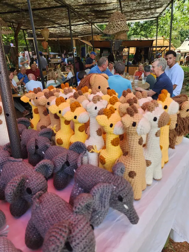 Crocheted giraffes and elephants on a white table at a busy open air thatched restaurant with seated diners