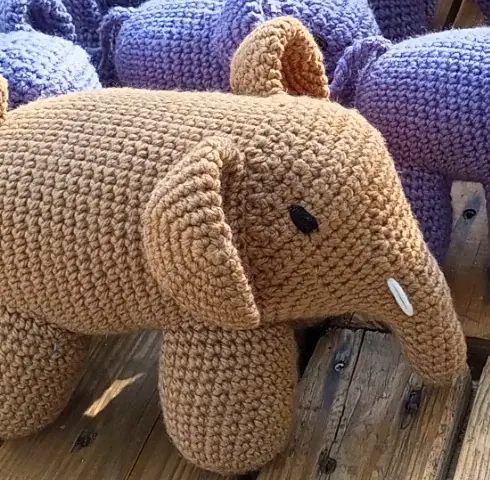 Caramel brown crocheted elephant with a white tusk on a wooden table