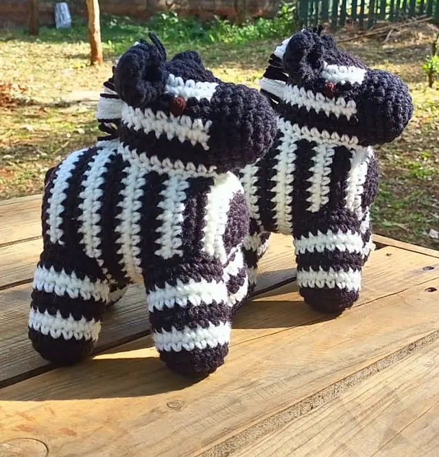 Two black and white striped crocheted zebras standing on a wooden table outdoors