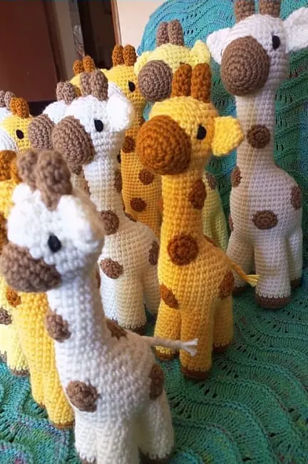 Crocheted yellow and white giraffes with brown spots standing close together on a teal blanket