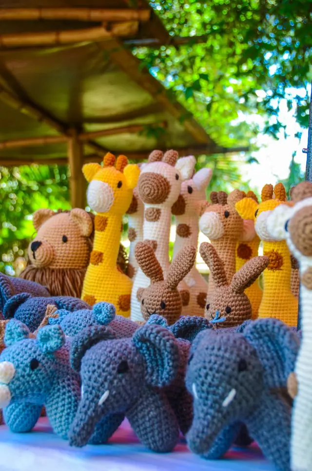 Yellow and cream giraffes, brown rabbits and blue elephants under a bamboo roof with green leaves behind