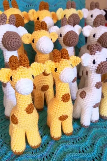 Crocheted giraffes in yellow and cream with brown spots and white muzzles, standing together on a teal blanket