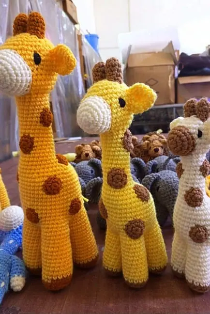 Three crocheted giraffes in different sizes and shades of yellow and cream standing together
