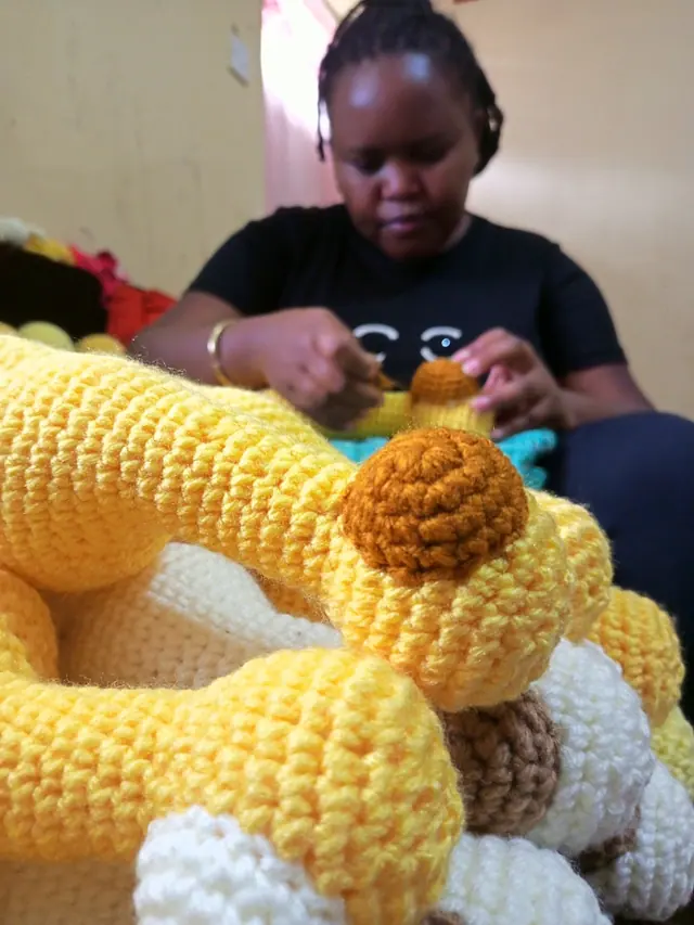 Young woman in a black t-shirt stitching crocheted yellow giraffe pieces, ready to assemble