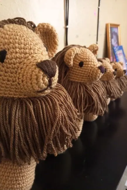 Close view along a line of crocheted tan lions on a dark table, the nearest one large and the others smaller