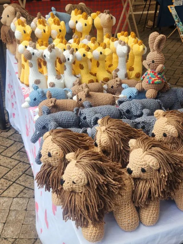 Table with crocheted lions at the front and rows of yellow and cream giraffes at the back