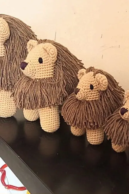 Row of crocheted tan lions with brown manes on a dark table, getting smaller from left to right